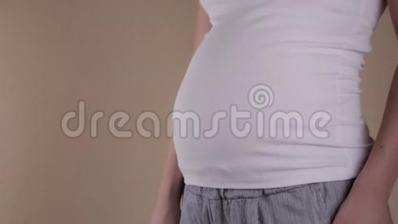 一个穿着白色T恤的孕妇腹部的特写镜头她用双手抱着她的腹部形成一个视频的预览图