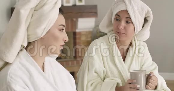 两名白人女性穿着浴袍和发巾坐在沙发上说话的肖像年轻漂亮视频的预览图
