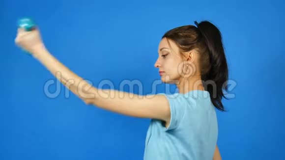 漂亮的年轻运动女性手中有哑铃在蓝工作室背景下做运动一个漂亮的女孩视频的预览图