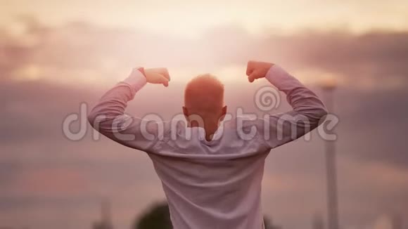强壮的肌肉男举起手显示出强大的庆祝胜利惊人的日落天空背景视频的预览图