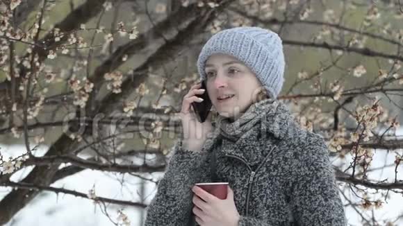 年轻女子在打电话手里拿着纸杯开花的树雪视频的预览图