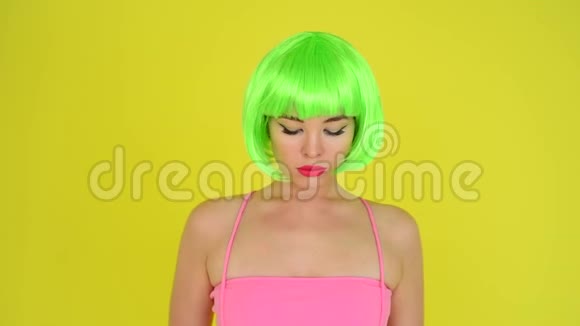 美丽的女人戴着绿色的短假发和粉红色的比基尼在黄色的背景上摆姿势一个性感的红色女孩的肖像视频的预览图