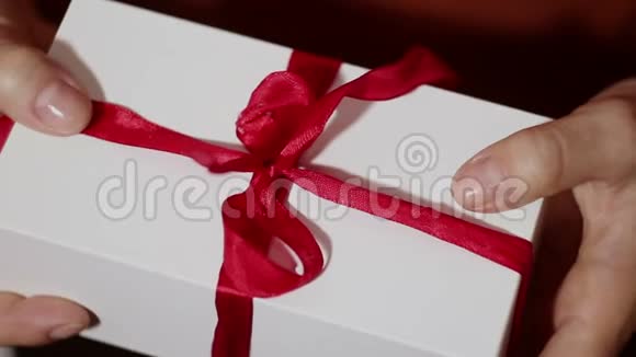 美丽的女孩打开她的礼物美丽的双手打开一个女孩新年礼物解开一条红丝带假期的礼物礼品视频的预览图