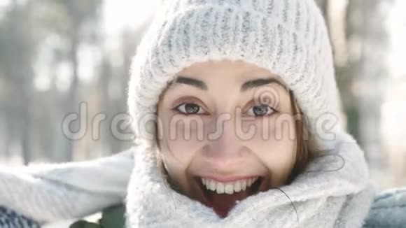 在白雪皑皑的冬季公园里穿着温暖的羊毛帽和长围巾的美丽欢笑的年轻女子慢镜头特写视频的预览图