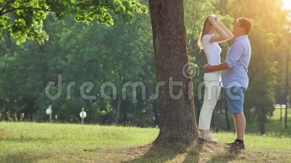 一个年轻的男人和女人站在公园的一棵树下拥抱视频的预览图