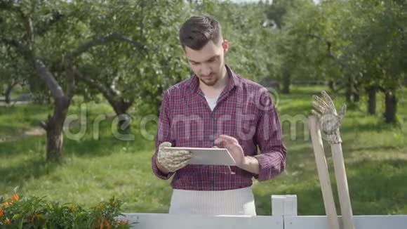 有经验成功和专业的园丁用平板电脑站在前景的篱笆后面视频的预览图