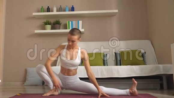 运动健身服中的美丽自信健身女孩正在客厅做伸展瑜伽运动视频的预览图
