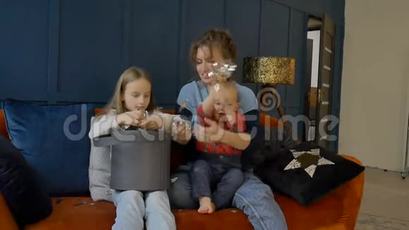 年轻的母亲女儿和儿子在家里坐在橙色的沙发上庆祝节日或生日视频的预览图