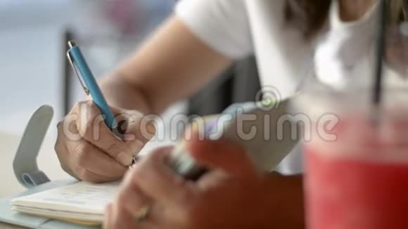 亚洲女人坐着写日记用一杯冰沙果汁激励饮料店的生活视频的预览图
