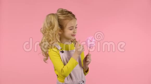 漂亮的女孩正在品尝棒子上的粉红色糖果视频的预览图