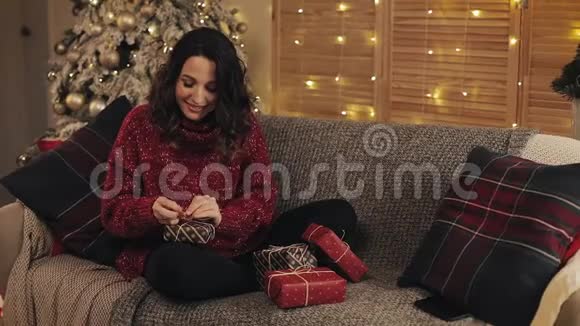 美丽的年轻女性完成圣诞礼物乐队磁带和绑在碗坐在沙发上接近圣诞节视频的预览图