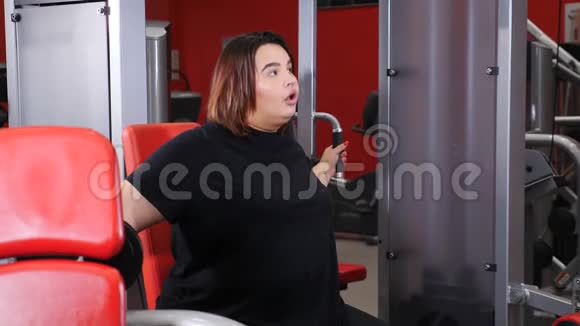 胖女人躺在健身房地板上拿着一块大蛋糕背景中的杠铃和各种健身机视频的预览图