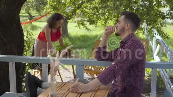 年轻的大胡子懒汉在前台喝茶而愤怒的迷人女孩穿着复古的衣服在视频的预览图