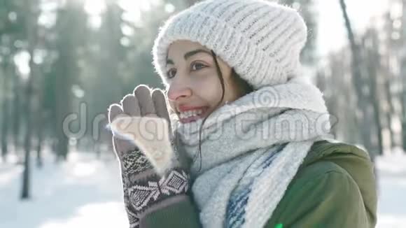 穿着羊毛帽戴着长长的暖围巾的美丽微笑的女子在雪地冬季公园的模糊的极端特写镜头视频的预览图