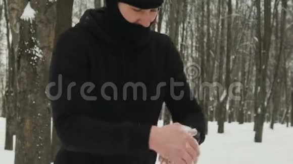 一个穿着黑色运动服和帽子的男人在冬天擦着手里沾满汗水的雪视频的预览图