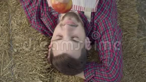 年轻人躺在干草上吃新鲜苹果的特写镜头农夫下班后休息农村生活方式视频的预览图