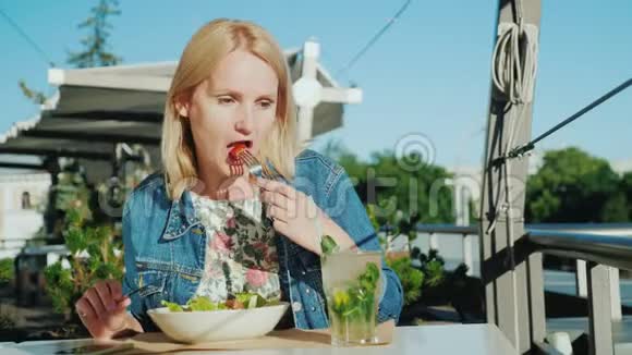 一个年轻的女人正在一家餐馆的夏季露台上吃沙拉吃户外用品视频的预览图