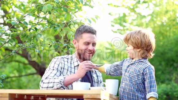 小男孩和英俊的父亲在花园里吃早餐为人父母为家庭提供食物和饮料快乐的父亲视频的预览图