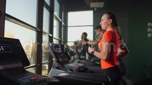 可爱的年轻女孩在健身房全景视窗前的跑步机上跑步带跑步机和大型健身房视频的预览图