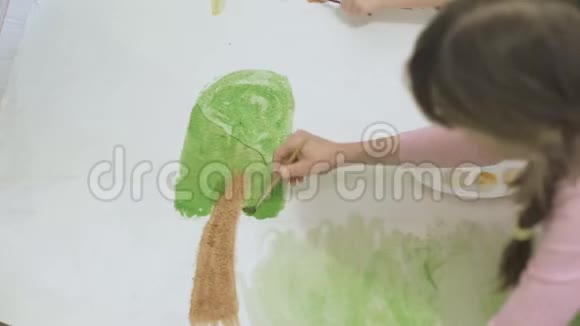 两个女孩在地板上用水彩颜料和画笔在一张大画纸上画画孩子们共同的创造力视频的预览图