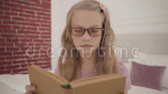 年轻聪明的少女戴着眼镜在家看书聪明的白人金发女学生在室内学习视频的预览图