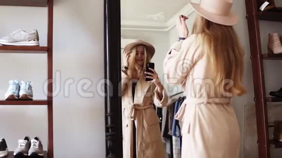 时尚的金发女孩站在镜子前穿着米色外套和时髦的帽子和她一起拍了一张照片视频的预览图