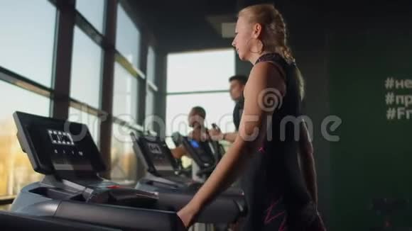 一个年轻漂亮的女孩走在跑步机上在一个大的全景窗口前慢动作背景视频的预览图