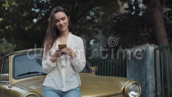 年轻貌美的白种人布鲁内特学生女孩使用手机应用和微笑时坐在老式视频的预览图