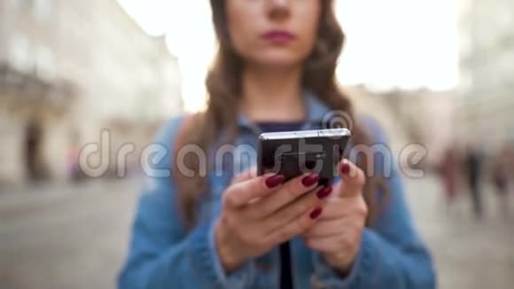 日落时分女人用智能手机走在老街上专注于智能手机通信社交网络在线视频的预览图