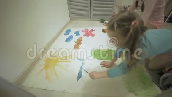 两个女孩在地板上用水彩颜料和画笔在一张大画纸上画画孩子们共同的创造力视频的预览图