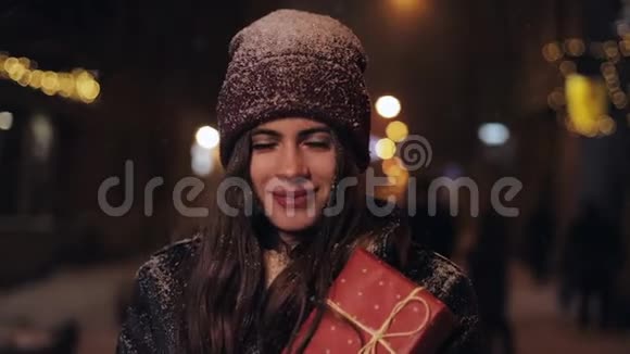 特写冬帽和手套中年轻快乐迷人女孩的肖像举着礼物盒站在坠落中视频的预览图