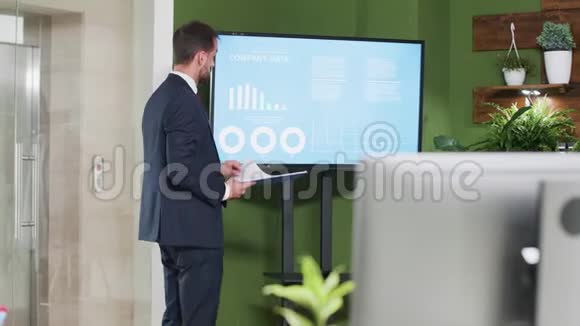 一位白人商人站在大屏幕电视旁视频的预览图