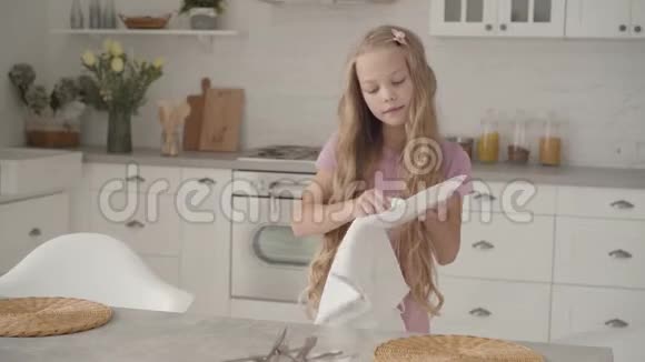 年轻的白种人十几岁的女孩穿着粉红色的连衣裙在现代厨房擦拭盘子看着一边叹息可爱的金发女郎视频的预览图
