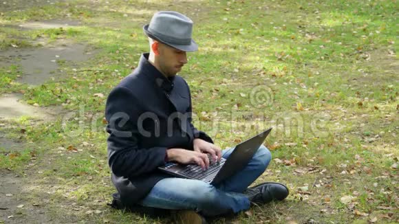 一个穿着外套戴着帽子的人坐在空地上拿着笔记本电脑打字视频的预览图