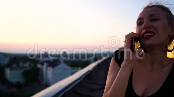日落时分一位带着发带在屋顶上打电话的年轻美女的画像视频的预览图