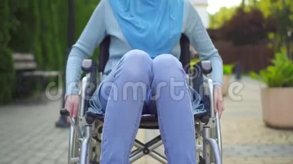 在公园里坐在轮椅上戴着传统围巾的年轻穆斯林女子微笑着展示双手视频的预览图