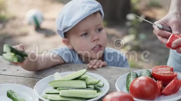 一个4岁的男孩看着妈妈把西红柿和黄瓜切成野餐沙拉视频的预览图