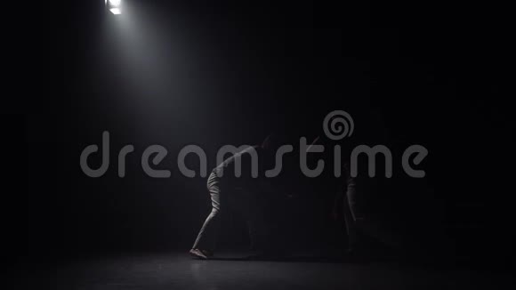 田径运动员在黑暗中练习卡波伊拉对抗演播室的聚光灯视频的预览图