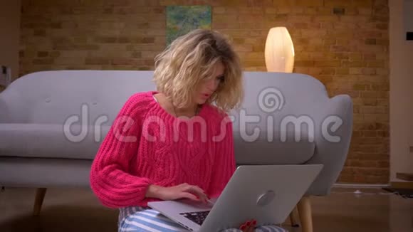 家庭主妇穿着粉红色毛衣在笔记本电脑中专注地冲浪在家庭氛围中全神贯注视频的预览图
