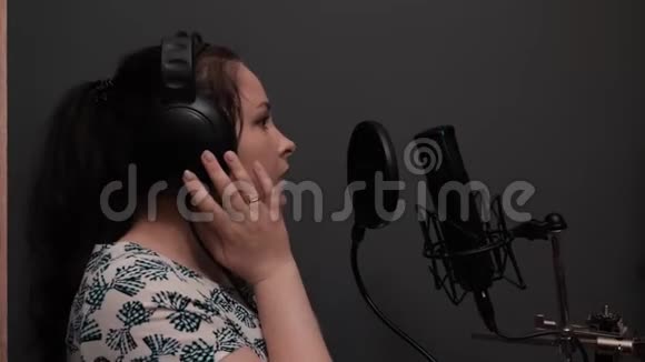 浪漫流行迪斯科女歌手开始唱歌戴耳机的女孩正在专业录音室排练歌曲视频的预览图