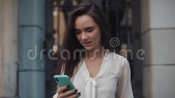 年轻漂亮的布鲁内特女孩在科西老城建筑后台行走时使用她的电话说哇微笑和微笑视频的预览图