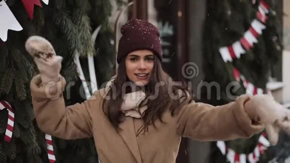 年轻快乐穿着冬装的迷人女孩站在外面飘落的雪花中微笑着跳舞着恳求天气视频的预览图