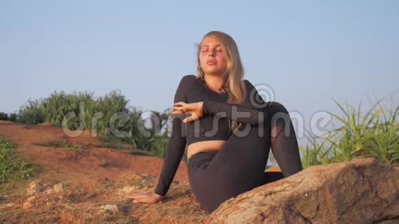 穿黑色运动服的漂亮女孩坐在灰色岩石悬崖上视频的预览图