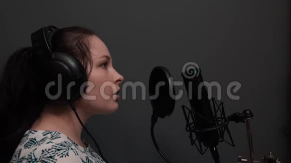 年轻迷人的流行女明星戴着耳机对着麦克风唱歌可爱的女孩在录音室表演歌曲音乐录音视频的预览图