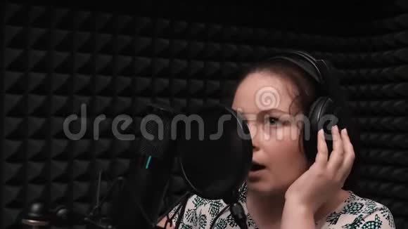 一个蓝眼睛的黑发少女有魅力的女人在录音室对着麦克风唱歌视频的预览图