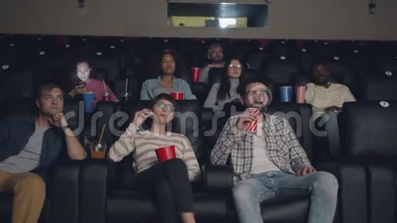 轻松的年轻人在电影院欣赏电影吃爆米花喝酒玩得开心视频的预览图
