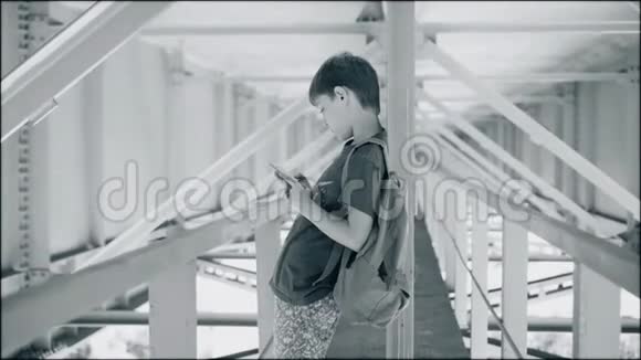 那个男孩站在一条凉爽的金属走廊里大气镜头男孩看着智能手机它在桥下视频的预览图