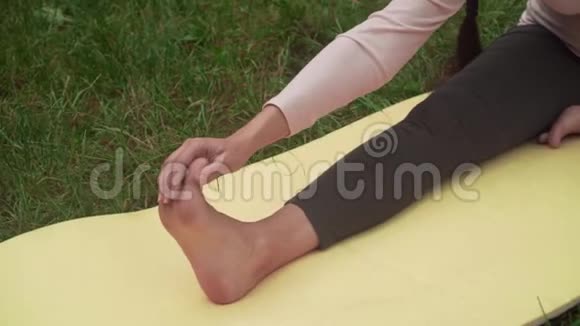 孕妇在公园里的地毯上做瑜伽一条腿伸着坐着做一个手对脚的倾斜视频的预览图