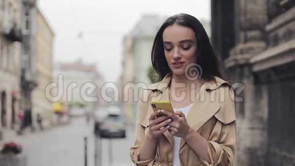 年轻的少女手持手机发短信笑着站在城市背景下视频的预览图