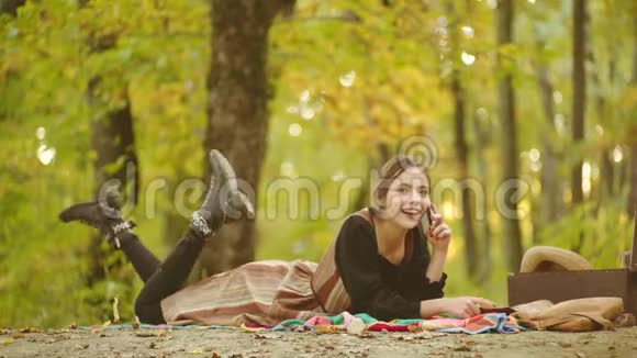 秋天公园的女模特带着手机快乐的女人时髦的人在智能手机上听音乐年轻女性玩得开心视频的预览图